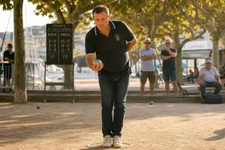 Pétanque player focused before throwing a boule on a sunlit, tree-lined boulodrome with a relaxed Provençal atmosphere