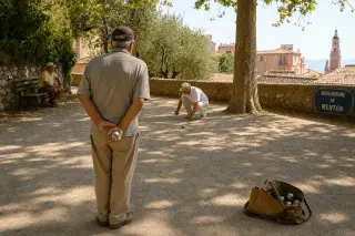 Pétanque player prepares to throw a boule on a sunlit, dusty terrain with plane trees, bag of boules open nearby, and warm Provençal afternoon light.